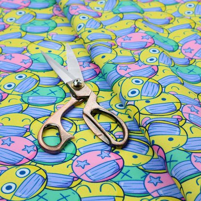 Seamless novelty fabric pattern featuring a dense, overlapping collage of cartoon emoji smiley faces wearing blue face masks in bright neon yellow, green, and pink.
