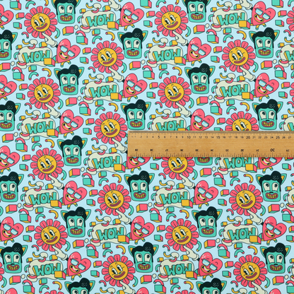 Seamless light blue fabric pattern featuring a busy retro cartoon collage with smiling flowers, heart characters, pompadour men, and "WOW" comic speech bubbles.