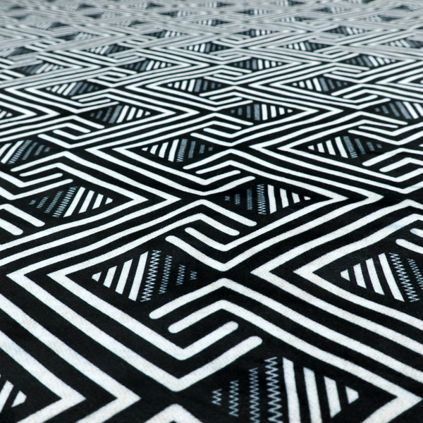 A geometric pattern featuring a repeating labyrinthine or Greek key-inspired design. The fabric has a high-contrast black and white colour scheme, with white interlocking lines forming diamond shapes and diagonal pathways against a deep black background.