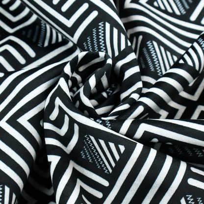 A geometric pattern featuring a repeating labyrinthine or Greek key-inspired design. The fabric has a high-contrast black and white colour scheme, with white interlocking lines forming diamond shapes and diagonal pathways against a deep black background.