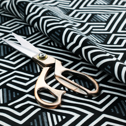 A geometric pattern featuring a repeating labyrinthine or Greek key-inspired design. The fabric has a high-contrast black and white colour scheme, with white interlocking lines forming diamond shapes and diagonal pathways against a deep black background.