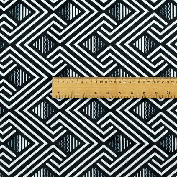 A geometric pattern featuring a repeating labyrinthine or Greek key-inspired design. The fabric has a high-contrast black and white colour scheme, with white interlocking lines forming diamond shapes and diagonal pathways against a deep black background.