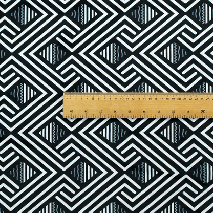 A geometric pattern featuring a repeating labyrinthine or Greek key-inspired design. The fabric has a high-contrast black and white colour scheme, with white interlocking lines forming diamond shapes and diagonal pathways against a deep black background.