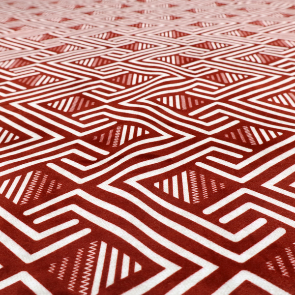 A bold geometric pattern featuring an interlocking labyrinth or fretwork design. The fabric is set in a striking terracotta red and cream colour palette, where crisp white lines weave together to form diagonal chains and diamond shapes against a rich, earthy red background.