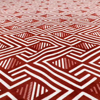 A bold geometric pattern featuring an interlocking labyrinth or fretwork design. The fabric is set in a striking terracotta red and cream colour palette, where crisp white lines weave together to form diagonal chains and diamond shapes against a rich, earthy red background.