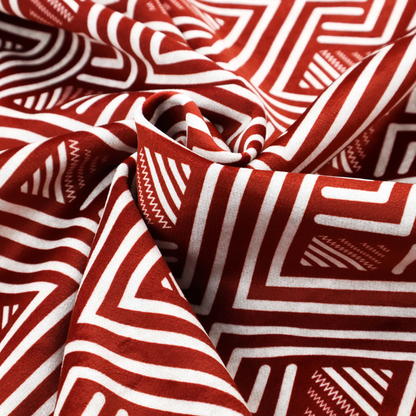 A bold geometric pattern featuring an interlocking labyrinth or fretwork design. The fabric is set in a striking terracotta red and cream colour palette, where crisp white lines weave together to form diagonal chains and diamond shapes against a rich, earthy red background.
