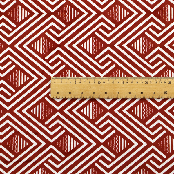 A bold geometric pattern featuring an interlocking labyrinth or fretwork design. The fabric is set in a striking terracotta red and cream colour palette, where crisp white lines weave together to form diagonal chains and diamond shapes against a rich, earthy red background.