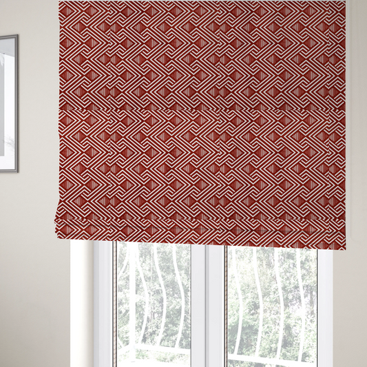 The fabric used to create these Roman blinds is a bold geometric pattern featuring an interlocking labyrinth or fretwork design. The fabric is set in a striking terracotta red and cream colour palette, where crisp white lines weave together to form diagonal chains and diamond shapes against a rich, earthy red background.