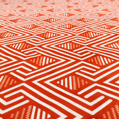A vibrant geometric pattern with a repeating labyrinth or fretwork motif. The fabric is designed in a high-energy orange and white colour palette, with crisp white interlocking lines creating diagonal paths and diamond shapes against a bright, warm orange background.