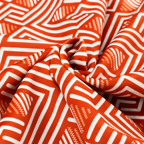 A vibrant geometric pattern with a repeating labyrinth or fretwork motif. The fabric is designed in a high-energy orange and white colour palette, with crisp white interlocking lines creating diagonal paths and diamond shapes against a bright, warm orange background.