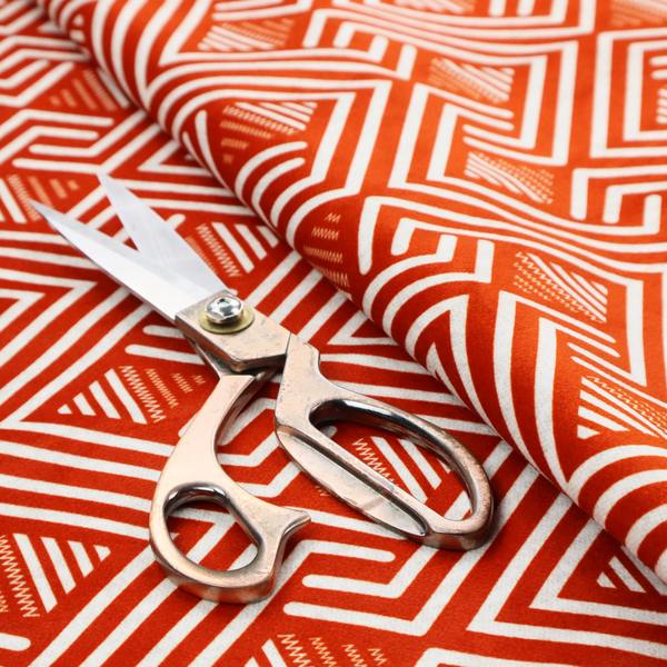 A vibrant geometric pattern with a repeating labyrinth or fretwork motif. The fabric is designed in a high-energy orange and white colour palette, with crisp white interlocking lines creating diagonal paths and diamond shapes against a bright, warm orange background.