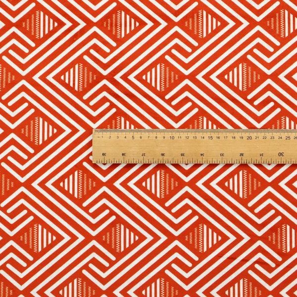 A vibrant geometric pattern with a repeating labyrinth or fretwork motif. The fabric is designed in a high-energy orange and white colour palette, with crisp white interlocking lines creating diagonal paths and diamond shapes against a bright, warm orange background.