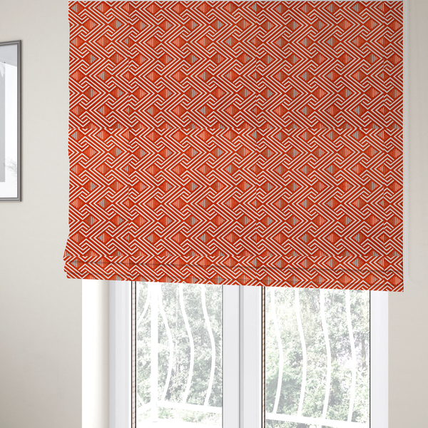 The fabric used to create these Roman blinds is a vibrant geometric pattern with a repeating labyrinth or fretwork motif. The fabric is designed in a high-energy orange and white colour palette, with crisp white interlocking lines creating diagonal paths and diamond shapes against a bright, warm orange background.