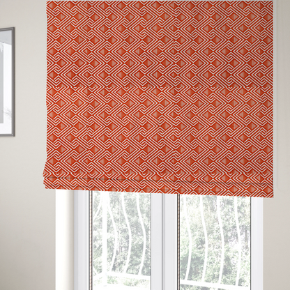The fabric used to create these Roman blinds is a vibrant geometric pattern with a repeating labyrinth or fretwork motif. The fabric is designed in a high-energy orange and white colour palette, with crisp white interlocking lines creating diagonal paths and diamond shapes against a bright, warm orange background.