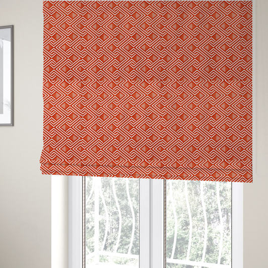 The fabric used to create these Roman blinds is a vibrant geometric pattern with a repeating labyrinth or fretwork motif. The fabric is designed in a high-energy orange and white colour palette, with crisp white interlocking lines creating diagonal paths and diamond shapes against a bright, warm orange background.