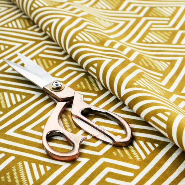 A dynamic geometric pattern with a repeating labyrinth or fretwork motif. The fabric showcases a sophisticated mustard yellow and white colour palette, with crisp white interlocking lines creating diagonal chains and diamond shapes against a warm, golden-yellow background.