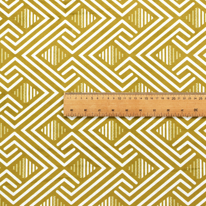 A dynamic geometric pattern with a repeating labyrinth or fretwork motif. The fabric showcases a sophisticated mustard yellow and white colour palette, with crisp white interlocking lines creating diagonal chains and diamond shapes against a warm, golden-yellow background.