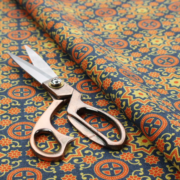 A dense, symmetrical textile pattern featuring a repeating grid of pale yellow eight-pointed stars and orange circular medallions. The motifs are interconnected by delicate orange scrolling vines and tiny floral accents, set against a deep navy blue background. The colour palette consists of mustard yellow, burnt orange, and indigo.