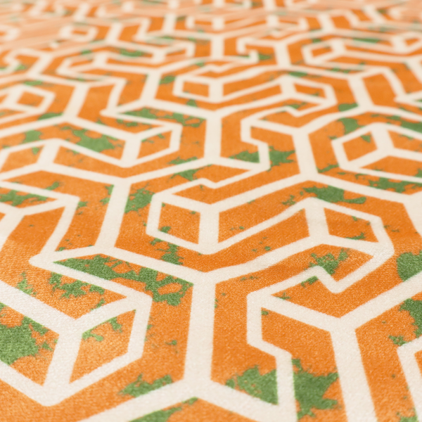 An orange and white textile fabric featuring a repeating, interlocking geometric pattern. The design consists of white outlines that form three-dimensional, maze-like structures or isometric blocks against a vibrant orange background. A textured, green moss-like speckled effect is scattered across the orange spaces, adding an organic contrast to the sharp, structured geometric lines.