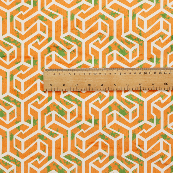 An orange and white textile fabric featuring a repeating, interlocking geometric pattern. The design consists of white outlines that form three-dimensional, maze-like structures or isometric blocks against a vibrant orange background. A textured, green moss-like speckled effect is scattered across the orange spaces, adding an organic contrast to the sharp, structured geometric lines.