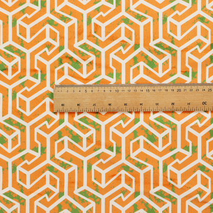 An orange and white textile fabric featuring a repeating, interlocking geometric pattern. The design consists of white outlines that form three-dimensional, maze-like structures or isometric blocks against a vibrant orange background. A textured, green moss-like speckled effect is scattered across the orange spaces, adding an organic contrast to the sharp, structured geometric lines.
