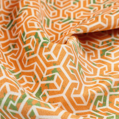 An orange and white textile fabric featuring a smaller, densely repeating interlocking geometric pattern. The design consists of fine white outlines forming complex, three-dimensional isometric block structures on an orange background. Scattered green, moss-like textured speckles are integrated throughout, creating an organic, weathered look against the sharp geometry.