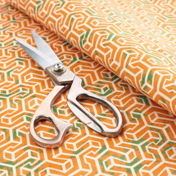 An orange and white textile fabric featuring a smaller, densely repeating interlocking geometric pattern. The design consists of fine white outlines forming complex, three-dimensional isometric block structures on an orange background. Scattered green, moss-like textured speckles are integrated throughout, creating an organic, weathered look against the sharp geometry.