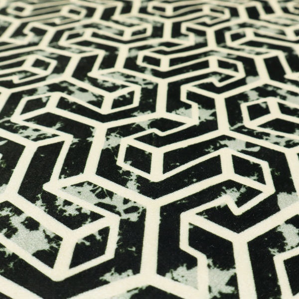 A black and off-white textile fabric featuring a repeating, interlocking geometric pattern. The design consists of off-white outlines that form three-dimensional, isometric maze-like structures against a solid black background. Distressed, pale green speckled textures are subtly integrated into the background spaces, giving the sharp, structured design a weathered, organic touch.
