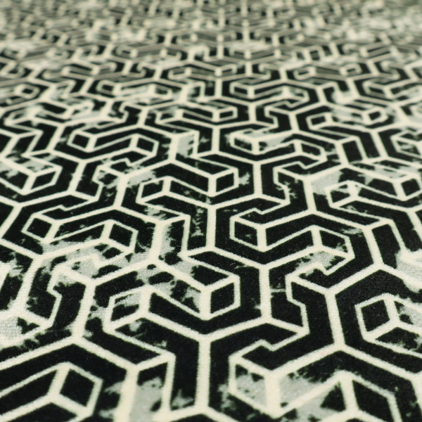 A black and off-white textile fabric featuring a small-scale, densely repeating interlocking geometric pattern. Fine off-white outlines construct complex, three-dimensional isometric block formations against a solid black background. Pale green, distressed textured speckles are integrated throughout, creating a weathered, organic contrast to the sharp geometric structure.