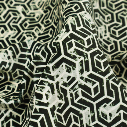 A black and off-white textile fabric featuring a small-scale, densely repeating interlocking geometric pattern. Fine off-white outlines construct complex, three-dimensional isometric block formations against a solid black background. Pale green, distressed textured speckles are integrated throughout, creating a weathered, organic contrast to the sharp geometric structure.