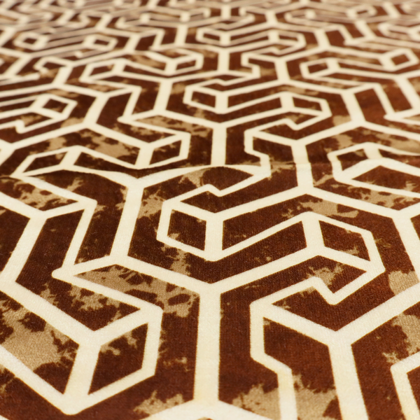 A brown and cream textile fabric featuring a repeating, interlocking geometric pattern. The design consists of cream-colored outlines forming three-dimensional, isometric maze-like structures against a warm, dark brown background. Lightly distressed, tan-speckled textures are subtly scattered throughout the brown spaces, adding a weathered, organic feel to the structured, geometric design.