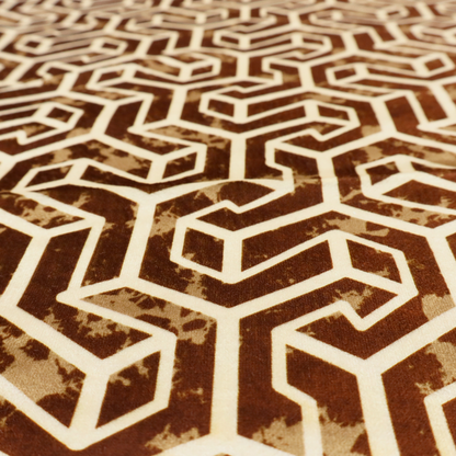 A brown and cream textile fabric featuring a repeating, interlocking geometric pattern. The design consists of cream-colored outlines forming three-dimensional, isometric maze-like structures against a warm, dark brown background. Lightly distressed, tan-speckled textures are subtly scattered throughout the brown spaces, adding a weathered, organic feel to the structured, geometric design.