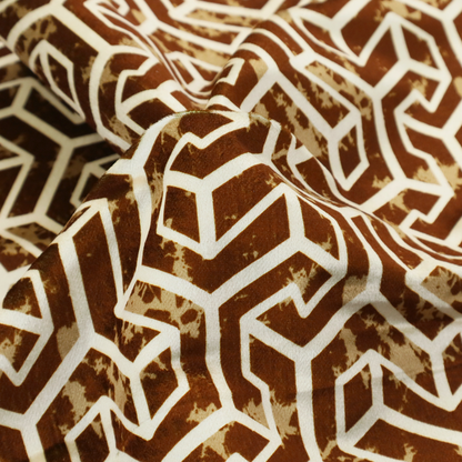 A brown and cream textile fabric featuring a repeating, interlocking geometric pattern. The design consists of cream-colored outlines forming three-dimensional, isometric maze-like structures against a warm, dark brown background. Lightly distressed, tan-speckled textures are subtly scattered throughout the brown spaces, adding a weathered, organic feel to the structured, geometric design.
