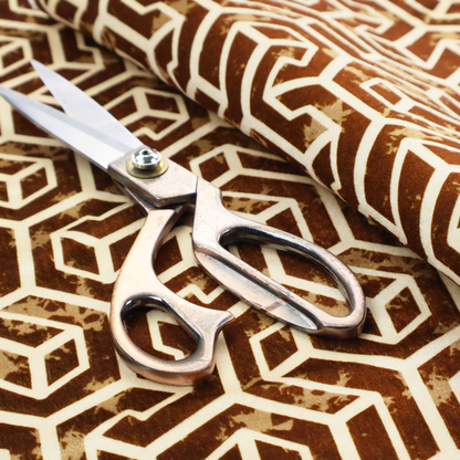 A brown and cream textile fabric featuring a repeating, interlocking geometric pattern. The design consists of cream-colored outlines forming three-dimensional, isometric maze-like structures against a warm, dark brown background. Lightly distressed, tan-speckled textures are subtly scattered throughout the brown spaces, adding a weathered, organic feel to the structured, geometric design.
