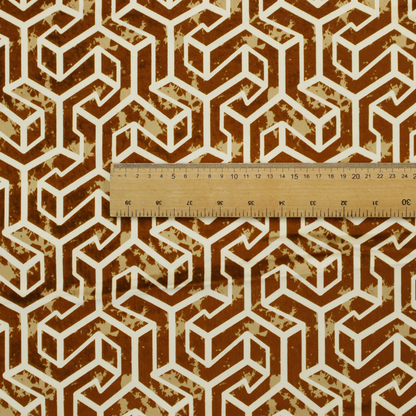 A brown and cream textile fabric featuring a repeating, interlocking geometric pattern. The design consists of cream-colored outlines forming three-dimensional, isometric maze-like structures against a warm, dark brown background. Lightly distressed, tan-speckled textures are subtly scattered throughout the brown spaces, adding a weathered, organic feel to the structured, geometric design.