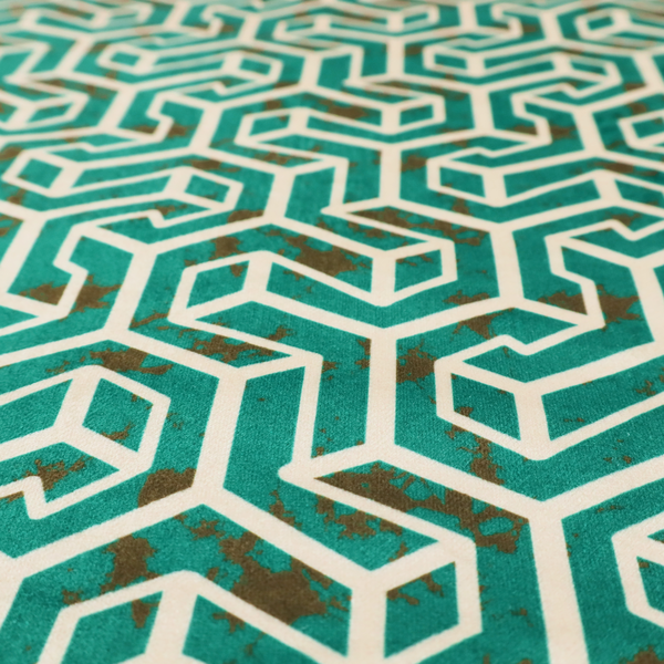 A teal and off-white textile fabric featuring a repeating, interlocking geometric pattern. The design consists of off-white outlines forming three-dimensional, isometric maze-like structures against a deep teal background. Distressed, brown speckled textures are subtly scattered throughout the teal spaces, giving the structured, geometric layout a weathered, organic touch.