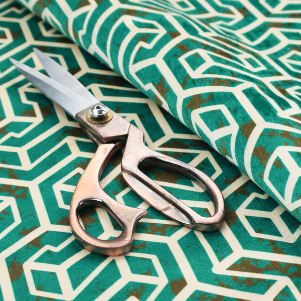 A teal and off-white textile fabric featuring a repeating, interlocking geometric pattern. The design consists of off-white outlines forming three-dimensional, isometric maze-like structures against a deep teal background. Distressed, brown speckled textures are subtly scattered throughout the teal spaces, giving the structured, geometric layout a weathered, organic touch.