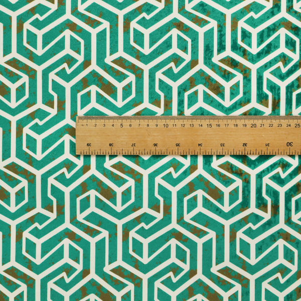 A teal and off-white textile fabric featuring a repeating, interlocking geometric pattern. The design consists of off-white outlines forming three-dimensional, isometric maze-like structures against a deep teal background. Distressed, brown speckled textures are subtly scattered throughout the teal spaces, giving the structured, geometric layout a weathered, organic touch.