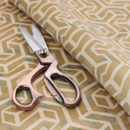 A beige and off-white textile fabric featuring a repeating, interlocking geometric pattern. The design consists of off-white outlines forming three-dimensional, isometric maze-like structures against a warm beige background. Distressed, pale green-blue speckled textures are subtly scattered throughout the beige spaces, giving the structured, geometric layout a weathered, organic touch.