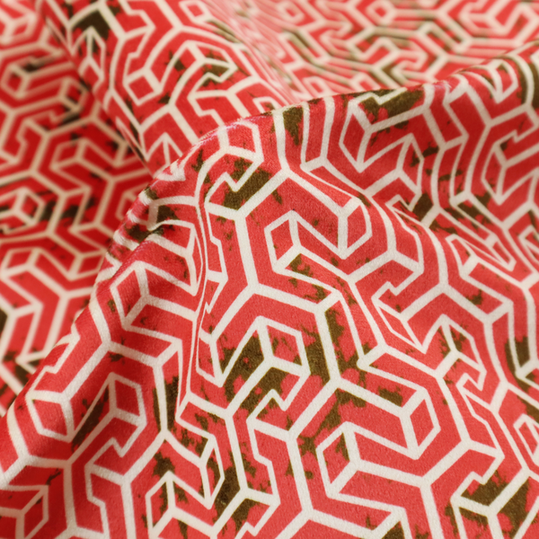 A coral red and off-white textile fabric featuring a small-scale, densely repeating interlocking geometric pattern. Fine off-white outlines construct complex, three-dimensional isometric block formations against a vibrant coral red background. Distressed, dark brown speckled textures are integrated throughout, creating a weathered, organic contrast to the sharp geometric structure.
