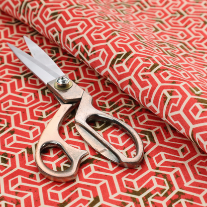 A coral red and off-white textile fabric featuring a small-scale, densely repeating interlocking geometric pattern. Fine off-white outlines construct complex, three-dimensional isometric block formations against a vibrant coral red background. Distressed, dark brown speckled textures are integrated throughout, creating a weathered, organic contrast to the sharp geometric structure.