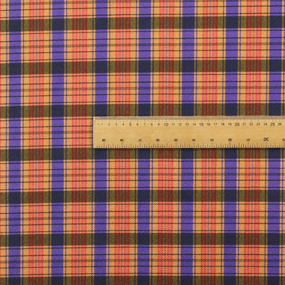 A vibrant, multi-coloured plaid fabric featuring a complex grid of horizontal and vertical stripes. The pattern blends deep indigo, golden ochre, and olive green, highlighted by thin, high-contrast stripes of bright violet and coral pink.