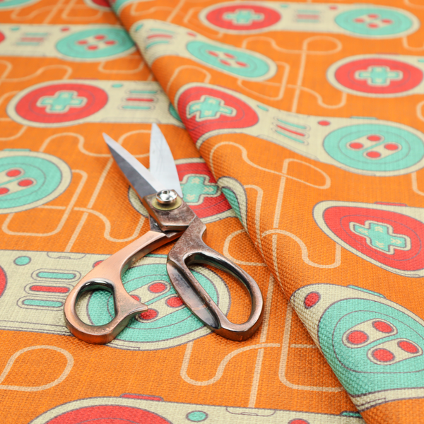 A playful, retro-inspired repeating fabric pattern featuring classic video game controllers connected by winding cord lines set against a warm orange background.