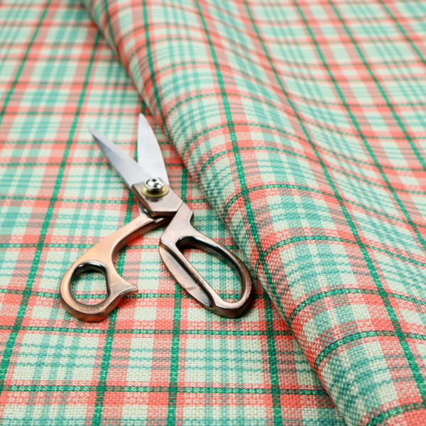 This fabric features a woven plaid pattern with a grid of intersecting horizontal and vertical stripes in coral, aqua, and dark green over a cream-colored background.