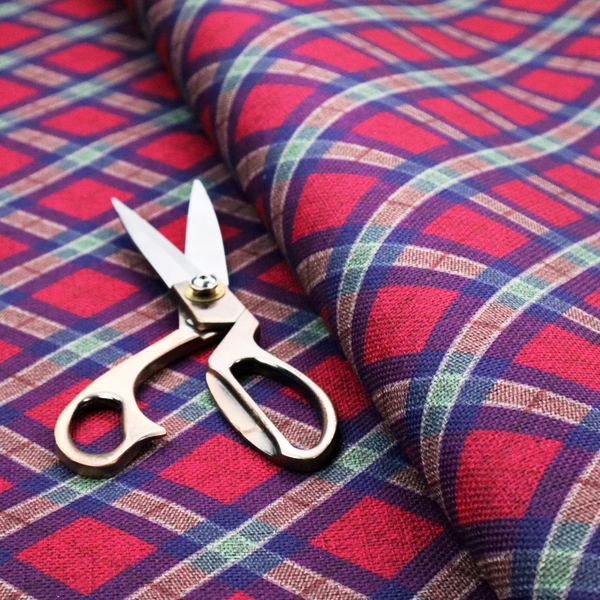 This fabric features a diagonal plaid pattern, creating a diamond-shaped grid. The design is composed of bold magenta squares framed by dark blue and thin white intersecting lines.
