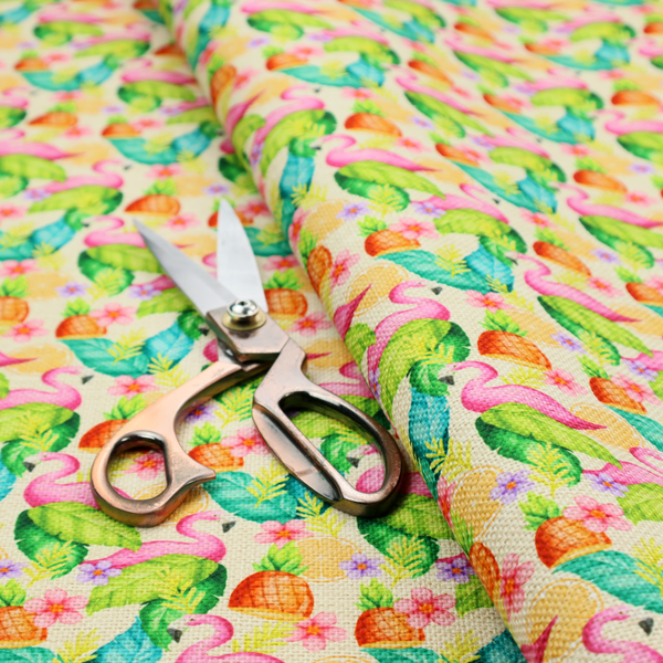This fabric features a tropical pattern on a light, neutral background, densely decorated with illustrations of bright pink flamingos, pineapples, lush green tropical leaves, and small purple and pink flowers.