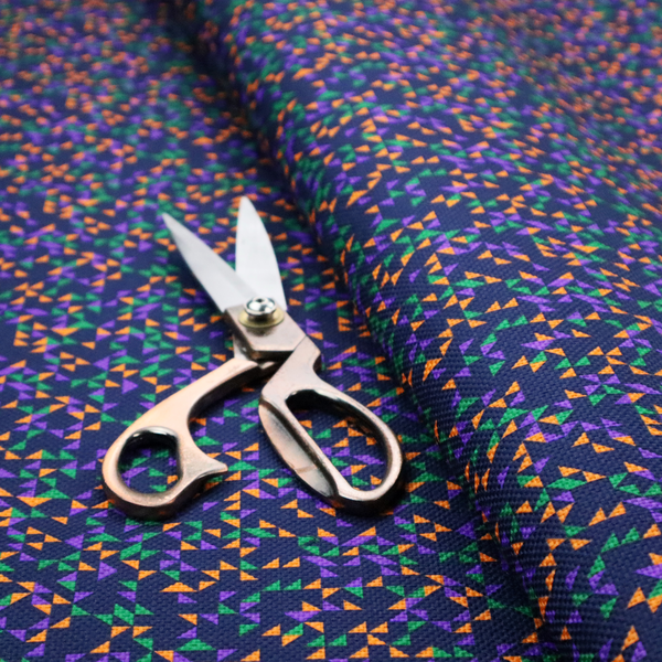 This fabric features a dense geometric pattern of tiny, randomly oriented triangles in shades of purple, green, and orange scattered across a solid dark navy blue background.