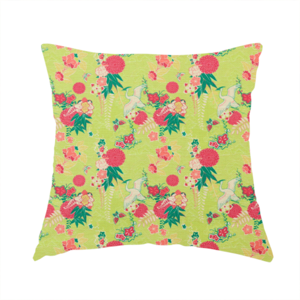 The fabric used to create this handmade cushion is a fabric features a whimsical, Chinoiseries-inspired pattern on a bright chartreuse-green background, repeating illustrations of white cranes, large dark pink pom-pom flowers, and leafy green ferns.