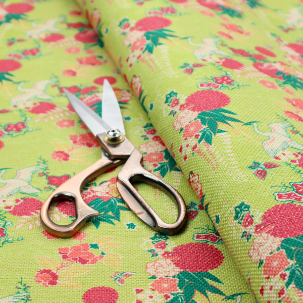 This fabric features a whimsical, Chinoiseries-inspired pattern on a bright chartreuse-green background, repeating illustrations of white cranes, large dark pink pom-pom flowers, and leafy green ferns.