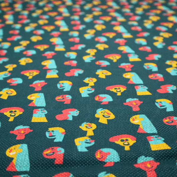 This fabric features a whimsical, repeating pattern on a dark teal background, decorated with stylized, colourful illustrations of diverse human faces in shades of bright yellow, light blue, and coral pink.